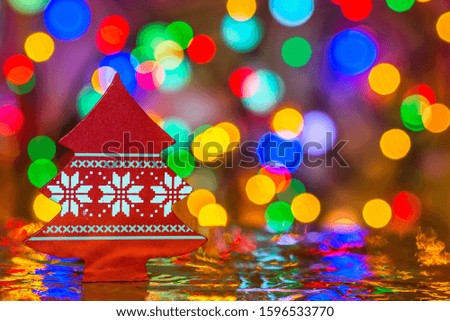 Red toy wooden Christmas tree on a blurred, sparkling and fabulous background. Holiday greeting cards. Minimalist composition. Colorful bokeh lights garland. The atmosphere of the New year. Copy space