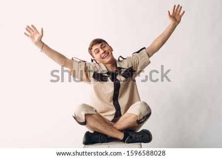 Young positive man sitting and smiling. Isolated on white background. Hands up.