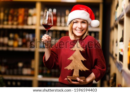 Picture of happy woman in Santa hat with glass and wooden tree in hands of store