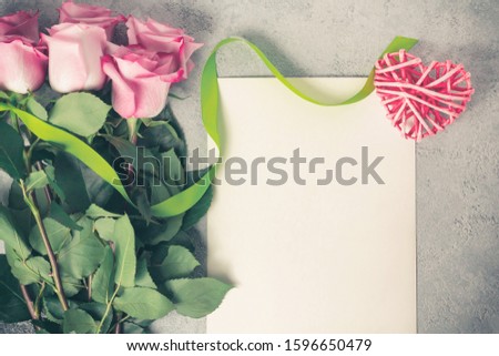 Flower arrangement - a bouquet of pink roses, a wicker heart and an empty sheet for inscription on a concrete surface, template for design or greeting card, top view, flat lay