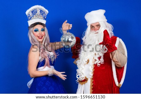 Emotional Santa Claus in a red coat and Snow Maiden in a blue suit with luminous ball posing on a blue background