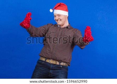 Young guy in a red cap and mittens Santa Claus poses on a blue background
