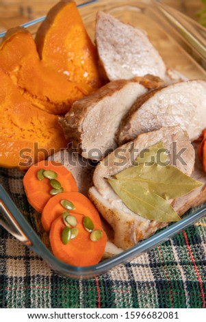 Sliced pork meat baked in the oven with pumpkin, carrots and pumpkin seeds, served in a glass transparent dish for baking on a green waffle napkin. Proper nutrition, diet, closeup.