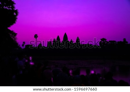 Tourist taking picture smartphone Angkor Wat temple Romantic Sunrise Purple silhouette reflection on water pond background. Holy place in Asain. Popular tourist attraction ancient temple.