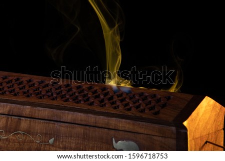 Smoke from incense sticks in a special Eastern wooden box. The fragrant smoke colored with  flashlight. Isolated in black. Smoke colored and photographed with high speed camera.