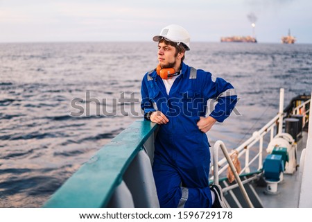 Marine Deck Officer or Chief mate seaman on deck of offshore vessel or ship , wearing PPE personal protective equipment - helmet, coverall looks at sea. ocean view Royalty-Free Stock Photo #1596729178