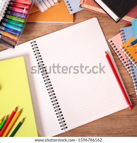 Busy student's desk with open notebook, school bag, text books and various pencils and crayons.