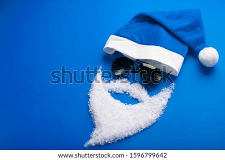 Cap, Santa Claus with black glasses and a beard of snow on a blue background. Merry Christmas Greeting card concept. The view from the top