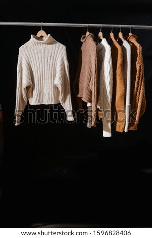 Different white and brown Knitted sweaters on hanger-black background
