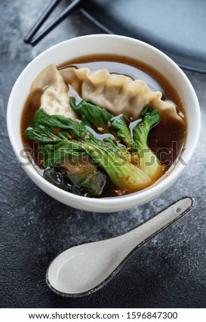 Bowl of asian dumpling soup with pak-choi over dark-grey stone background, vertical shot