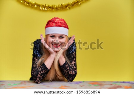 The concept of the New Year mood of a blonde girl sits at a table. Portrait of a woman in a business suit with long beautiful hair and excellent make-up with New Year's decor on a yellow background.