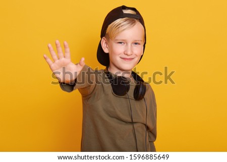 Handsome little boy standing isolated over yellow background showing and pointing up with fingers number five while smiling and looking directly t camera, looks confident and happy. Childhood concept.
