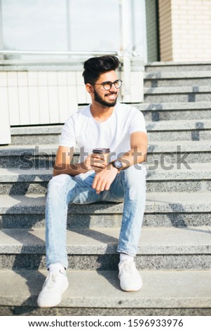 Young indian man drink coffee while sitting on the stairs in the street