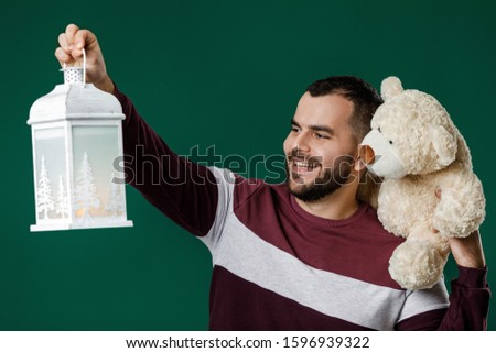 man tells a fairy tale. Bearded smiling man holding teddy bear and lantern on green background.