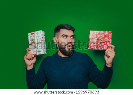 Happy bearded man in sweater holds many christmas gift boxes on the green background. Surprised man holds presents.