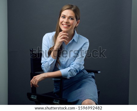 Woman in blue shirt and skirt sitting  relaxed on movie director chair.