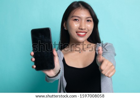 Young Asian woman show thumb up  with mobile phone on cyan background.