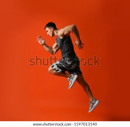 Athletic young man running on red background, side view