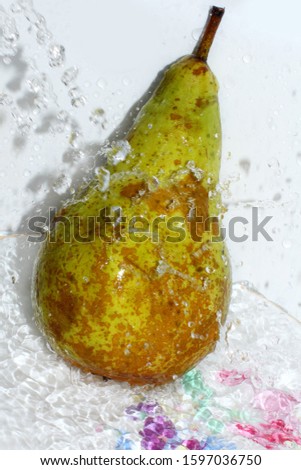 A ripe green pear is washed under running water with water splashes and drops. 