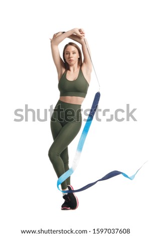 Slender girl gymnast in khaki sportswear performs with a blue ribbon, isolated on white background.