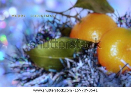 Merry Christmas greeting card with defocused blurred colorful bokeh light background of ripe mandarins with green leaves, tinsel and congratulations text. Decorative and holiday concept. 