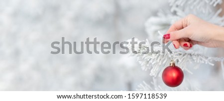 A female hand hangs a Christmas ball on a frozen branch in the winter forest on a blurry background. Christmas and New Year concept. Empty space for text