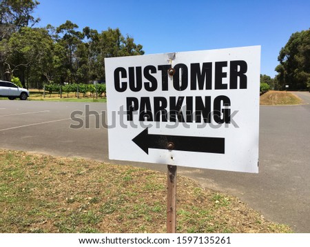 Sign indirecting customer parking to the left with bitumen road and vineyard in background - Margaret River, WA, Australia