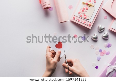 cropped view of woman cutting out heart with scissors near valentines decoration, gifts, hearts and wrapping paper on white background