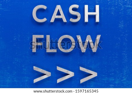 The words cash flow with arrows laid on blue painted board with thick silver metal aphabet characters.