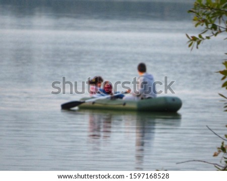 Defocused photo of a couple sailing in an inflatable boat shot from behind the bushes.  The girl in the boat takes pictures of the landscape on the phone.