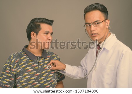 Young multi-ethnic man and young Indian man doctor against gray background