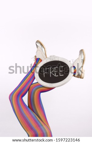 A female model's long legs are stretched out high in 
a vertical form in front of a white background. Her 
legs are decorated with a chalkboard sign with the
word free written on it.