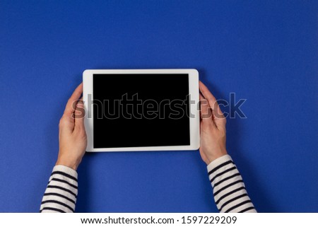 Female hands holding digital tablet computer on navy blue background. Top view