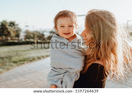 Close-up Portrait of Beautiful Mother Holding on Hands Cute Little Child in Towel. Positive Photo of Smiling Kid with Happy Parent on Summertime Holiday Happines Emotion Background