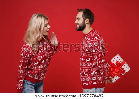 Funny young couple guy girl in Christmas sweaters posing isolated on red background. Happy New Year 2020 celebration holiday party concept. Mock up copy space. Hold present box with gift ribbon bow