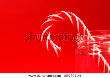 One Lollipop Candy cane in a glass jar on a red background.