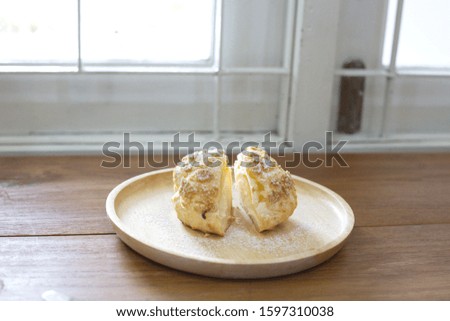 Choux Cream Eclair in a brown wooden plate on a brown wooden table by the white window