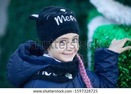 Portrait of a little girl in winter clothes near a green Christmas tree