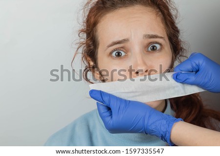 A Caucasian woman with sticky tape gluing her mouth. Hands in gloves hold a vow. The victim of violence is scared and cannot scream. Fear in eyes. The place for an inscription Royalty-Free Stock Photo #1597335547