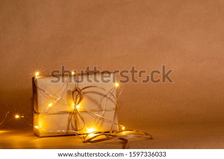 Square present wrapped with kraft paper and bow, in a rustic and simple manner, with shinning lights over a kraft paper color background. Minimalistic, Celebration concept, text space.