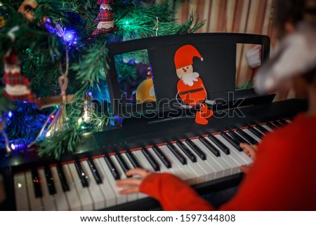 Cute little girl play Christmas melody on piano with support of diy paper santa Claus, merry Christmas celebration, focus on Santa, happy seasonal holidays