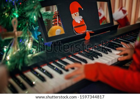 Cute little girl play Christmas melody on piano with support of diy paper santa Claus, merry Christmas celebration, focus on Santa, happy seasonal holidays