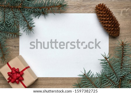 New Year or Christmas festive background. White sheet of paper with copy space, gift box and Christmas tree branches on wood. Flat lay, view from above