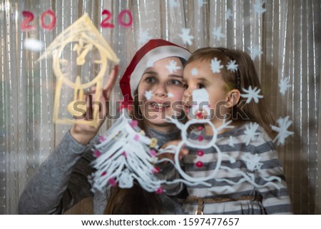 Mom and daughter draw a snowman, a Christmas tree and a clock with paints on a window pane. Drawing with acrylics on glass.