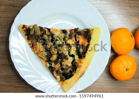 Small piece of pizza in a white plate on a wooden table with manadrins. Top view of a fruit still life with pastries and tropical fruits.