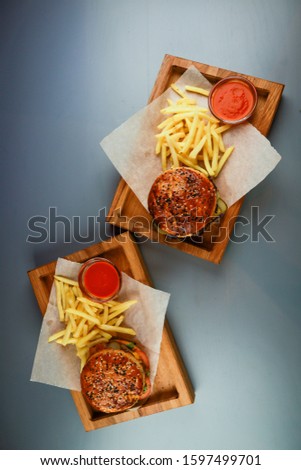 Two burgers with beef, chicken and french fries. Wooden plate. Gray background. Submission of the restaurant.