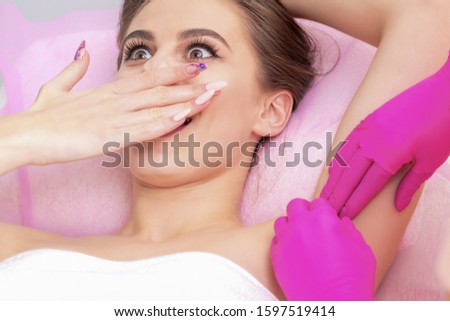 Young woman receives waxing epilation under her armpits, close up.