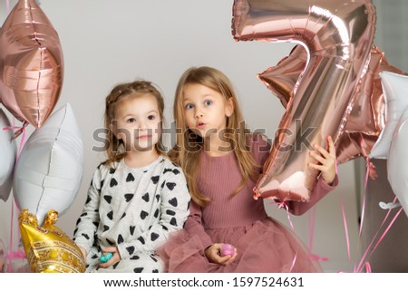 seven year old girl celebrates her birthday with little sister on a white background with seven balloons