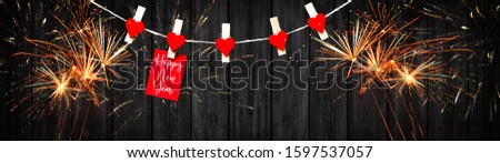 Happy New Year - Firework, Silvester - Clothes pegs with red wooden hearts and paper notes hang on rope isolated on black wooden texture background panorama banner long, with space for text