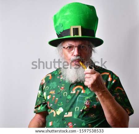 Old Caucasian man in a St Patrick's day costume smoking a meerschaum pipe and holding a green drink. 


